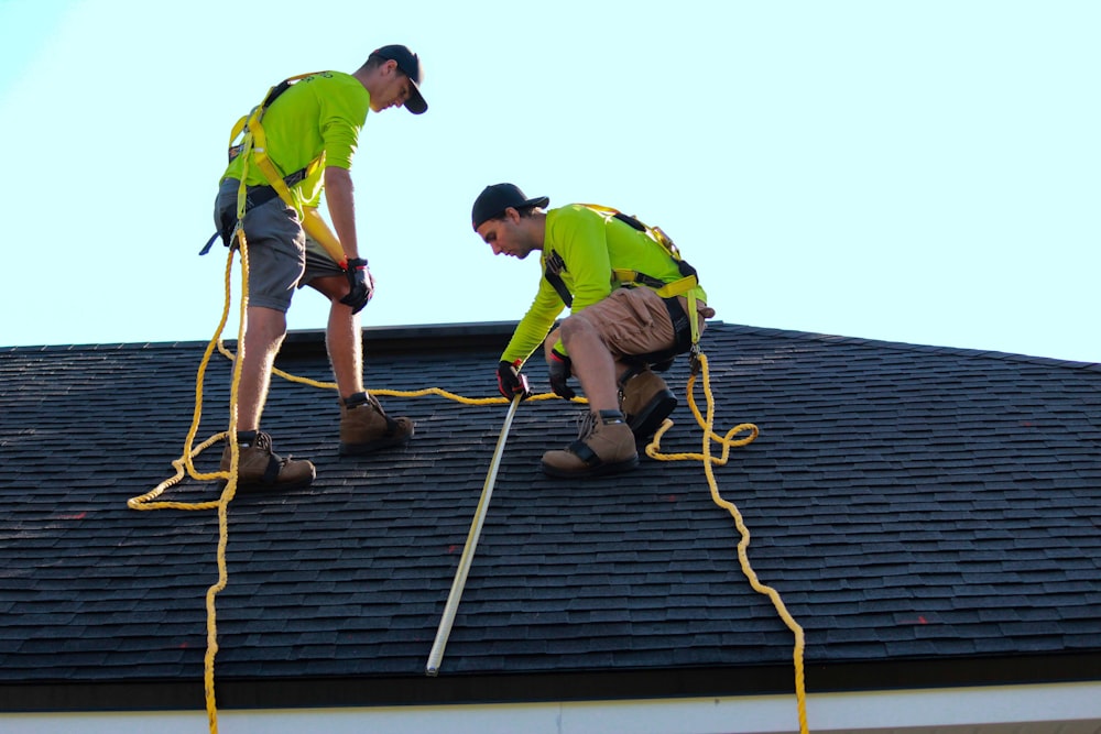 Two roofers in high-vis measuring a shingle ridge against a clear sky